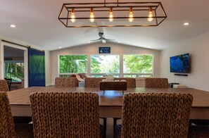 A conference room with a large table and chairs, a ceiling fan, and a view of trees through large windows. - Beach View Cottage - Beautiful View of the Lake! (Holland)