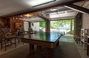 A ping pong table in a room with wooden walls and a garage door. - Beach View Cottage - Beautiful View of the Lake! (Holland)