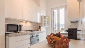 Una cucina moderna con mobili bianchi, forno a microonde, fornello, forno e un cesto di frutta sul bancone.