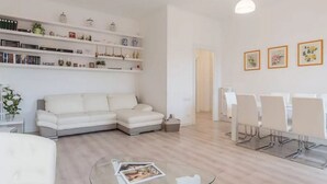 Un soggiorno moderno con un divano bianco, un tavolino in vetro e una zona pranzo con sedie bianche.