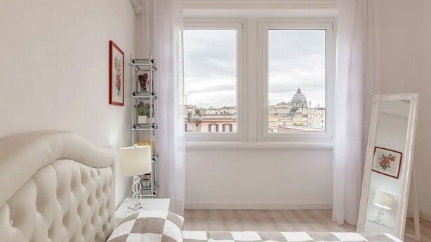 Una camera da letto con un letto grande, una finestra vista città, un comodino e uno specchio.