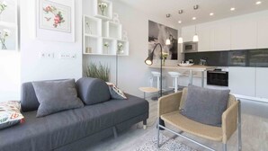 Un soggiorno moderno con un divano grigio, una poltrona in vimini e un angolo cottura con mobili bianchi e un forno a microonde nero.