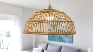 A room with a grey sofa, a hanging woven light fixture, and a painting on the wall.