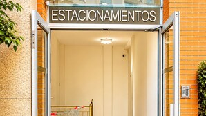 Entrada de un hotel con un cartel que dice 'ESTACIONamientos', un carrito de compras y una planta en maceta.