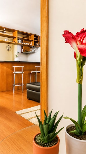 Une cuisine moderne avec des meubles en bois, un coin repas avec un canapé noir et deux plantes en pot.