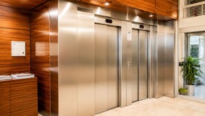 Un ascensor moderno con paneles de madera, una pantalla digital y una planta en maceta cerca de la entrada.