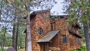 A rustic cabin with a sloped roof, a small porch, and a stack of firewood outside. - Sunriver Condo with Access to The Cove (Sunriver)