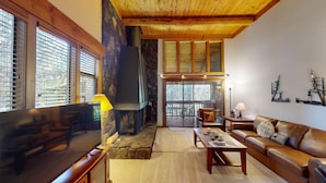 A cozy living room with a stone fireplace, wooden ceiling, and large windows. - Sunriver Condo with Access to The Cove (Sunriver)