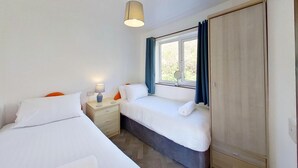 Ein Schlafzimmer mit zwei Betten, einem Nachttisch mit Lampe, einem Fenster mit Vorhängen und einem Kleiderschrank.