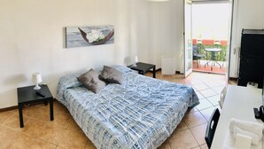 Un dormitorio con cama, mesitas de noche, lámpara, un cuadro y vistas al balcón exterior.