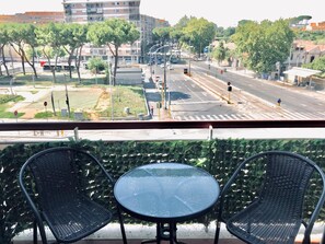 A balcony with two wicker chairs and a glass table, overlooking a city street with buildings and trees. - Alloggio turistico Lamberto Preneste (Rome)