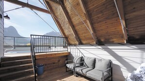 A wooden deck with a sofa and a small table, a staircase, and a view of mountains. - Basecamp Resorts Canmore I Micro-Suite, Dog Friendly (Canmore)