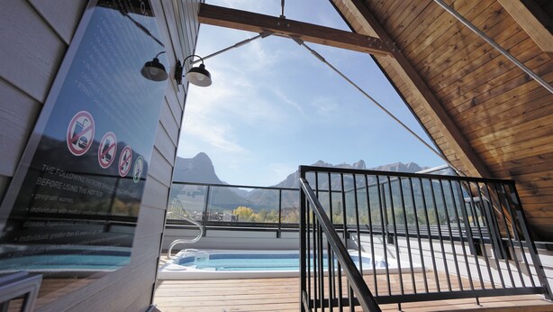 A hot tub area with a view of mountains, a wooden deck, and a sign with safety instructions. - Basecamp Resorts Canmore I Micro-Suite, Dog Friendly (Canmore)