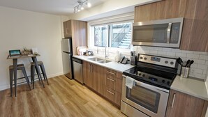 A modern kitchen with stainless steel appliances, wooden cabinets, and a window providing natural light. - Basecamp Resorts Canmore I Micro-Suite, Dog Friendly (Canmore)