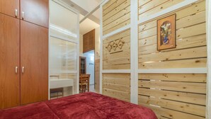 Un dormitorio con una colcha roja, un armario de madera y una pared de madera con un cuadro.