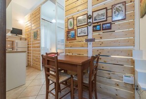 Un coin repas avec une table et des chaises en bois, une cuisine équipée d’un réfrigérateur et un mur orné de tableaux.