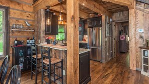A rustic kitchen with wooden beams, a bar area with stools, and modern appliances. - Riverbend Cabin! A Luxurious New Private Waterfront  Log Cabin. (Waynesville)