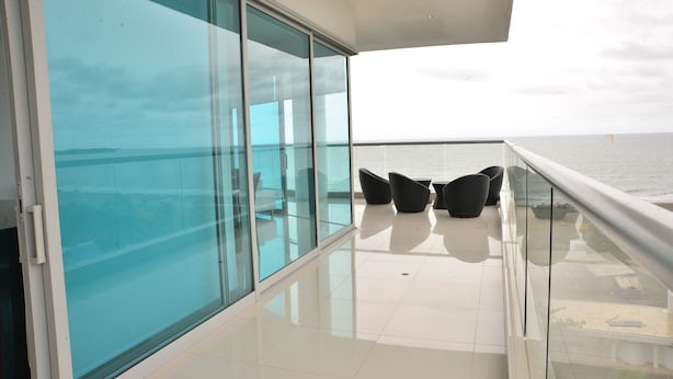 A balcony with a glass wall overlooking the sea, furnished with black chairs and a table. - APARTAMENTO AMPLIO 3 ALCOBAS FRENTE PLAY (Cartagena)