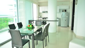 A modern kitchen with white cabinets, a refrigerator, and a dining area with a glass table and chairs. - APARTAMENTO AMPLIO 3 ALCOBAS FRENTE PLAY (Cartagena)
