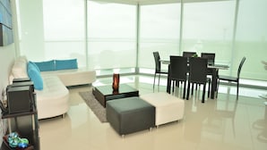 A modern living room with a white sofa, grey ottoman, and a glass dining table with chairs. - APARTAMENTO AMPLIO 3 ALCOBAS FRENTE PLAY (Cartagena)