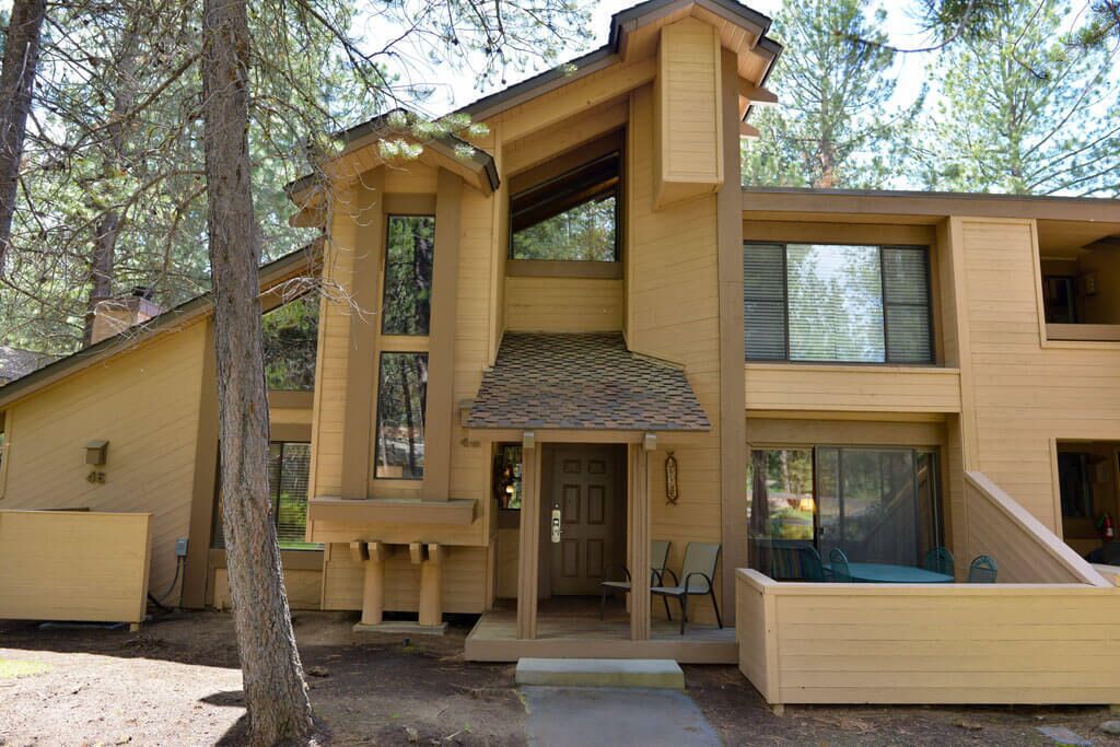 A modern two-story wooden house with a covered porch, large windows, and a small outdoor seating area.
