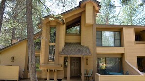 Ein modernes, zweistöckiges Holzhaus mit überdachter Veranda, großen Fenstern und einer kleinen Außenlounge.
