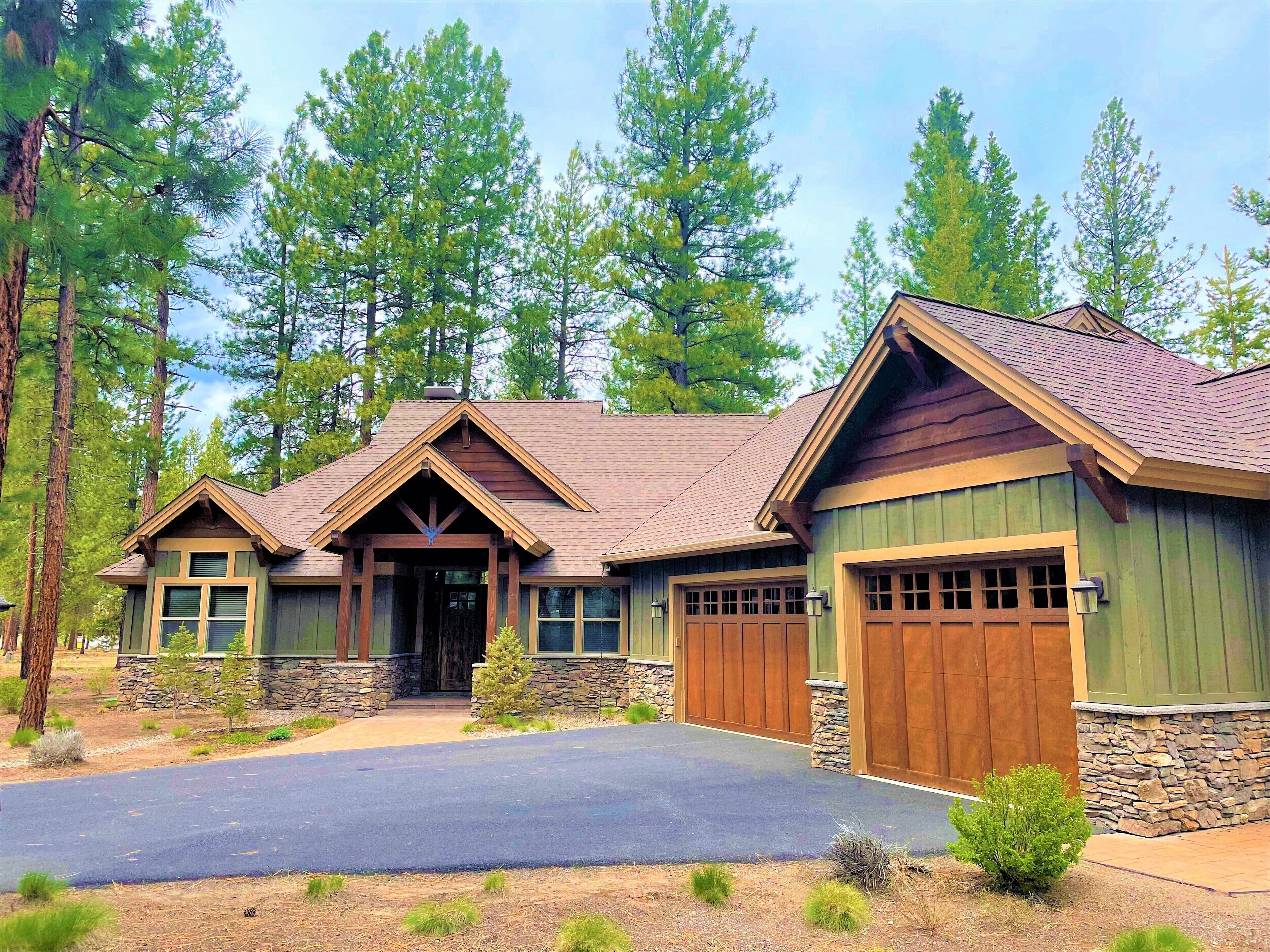 A two-story house with a stone foundation and wooden siding, surrounded by tall pine trees.