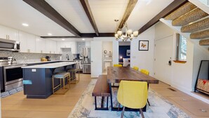 Una cucina moderna con isola centrale, elettrodomestici in acciaio inossidabile e zona pranzo con tavolo di legno e sedie gialle.