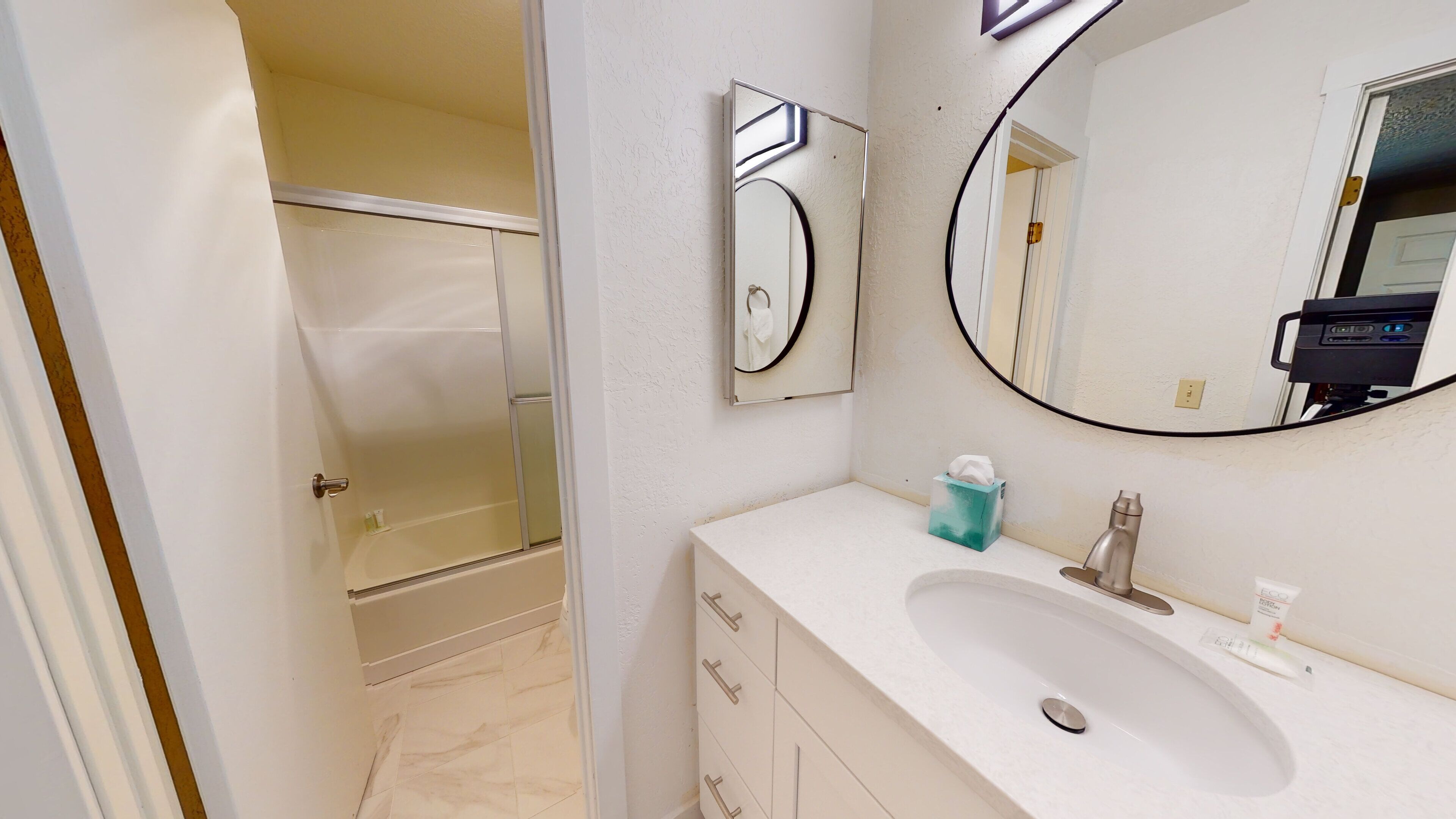 A bathroom with a bathtub, a sink, a mirror, and a towel dispenser.