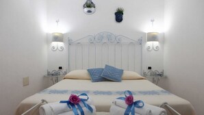 A hotel room with a bed, two wall-mounted lamps, a metal headboard, and two towels with ribbons on the bed. - B&B treatment in La Maddalena, Sardinia (La Maddalena)