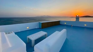A rooftop terrace with white furniture, a small table, and a view of the sunset over the sea. - Casa Del Mare - Unique Beachfront Cycladic Villa @ Agios Prokopios (Agios Prokopios)
