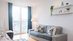 Uma sala de estar moderna com um sofá cinza, uma mesa de centro de vidro e vista para a cidade através de grandes janelas.