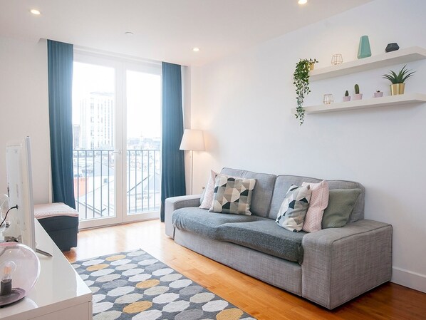 A modern living room with a grey sofa, a glass coffee table, and a view of the city through large windows.