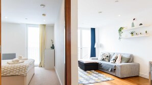 Quarto de hotel moderno com cama, sofá, pequena mesa e janela com cortinas.