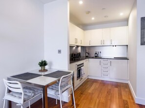 A compact kitchen with white cabinets, a dining table with chairs, and a small potted plant.