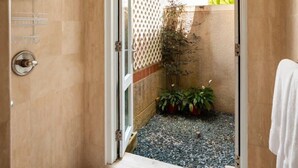 Een badkamer met een douchedeur die uitkomt op een klein buitengebied met planten en een houten schutting.