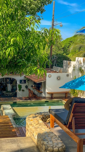 A pool area with a lounge chair, a stone wall, and a sign for 'MANTRAS'. - Casa de Olas Boutique Hotel (Puerto Escondido)