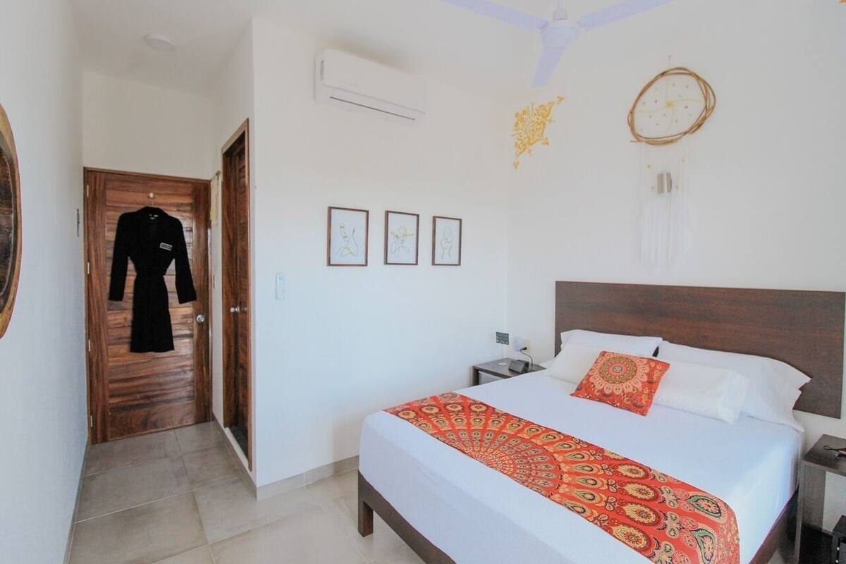 Una habitación de hotel con una cama, una mesita de noche, un reloj de pared y una puerta que da a otra habitación.