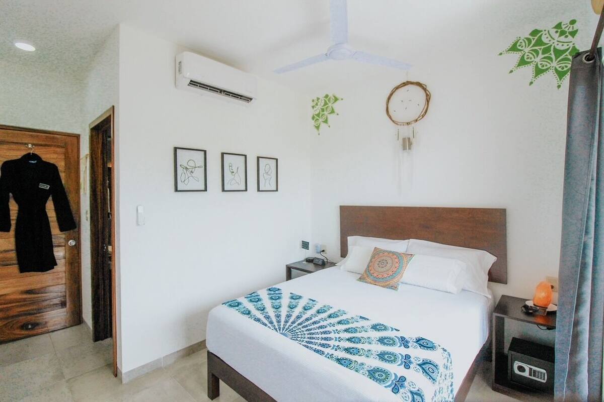 Habitación de hotel con cama, puerta de madera, aire acondicionado instalado en la pared, cuadros enmarcados y ventilador de techo.