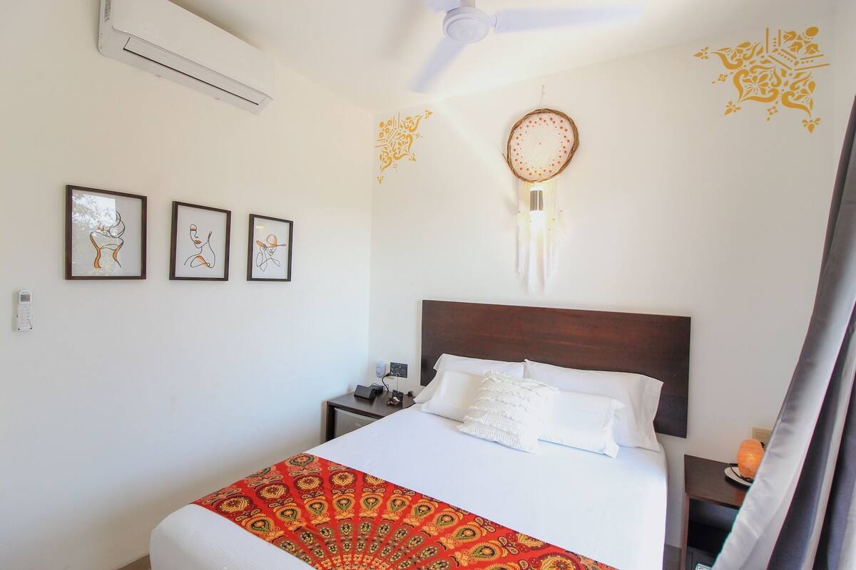 Una habitación de hotel con cama, mesita de noche, aire acondicionado instalado en la pared y decoración mural.