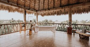 A spacious terrace with a thatched roof, a table set for dining, and a Buddha statue. - Casa de Olas Boutique Hotel (Puerto Escondido)
