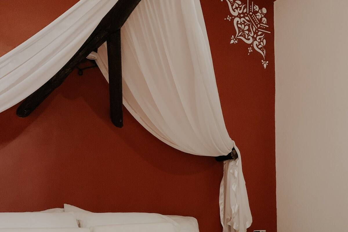 Un dormitorio con una cama, ropa de cama blanca, un tapete rojo estampado y un adorno de pared.