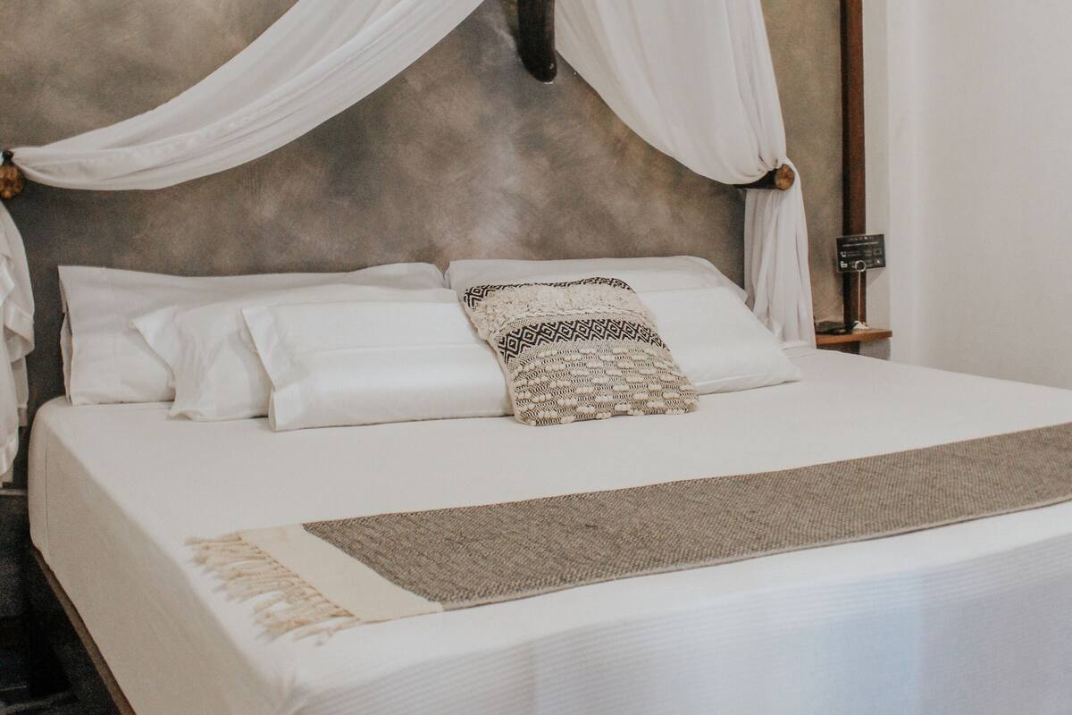 Una cama con dosel, ropa de cama blanca y un plaid estampado.