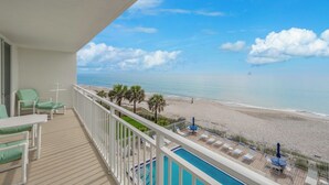 Ein Balkon mit Pool, Strandblick und Liegestühlen.