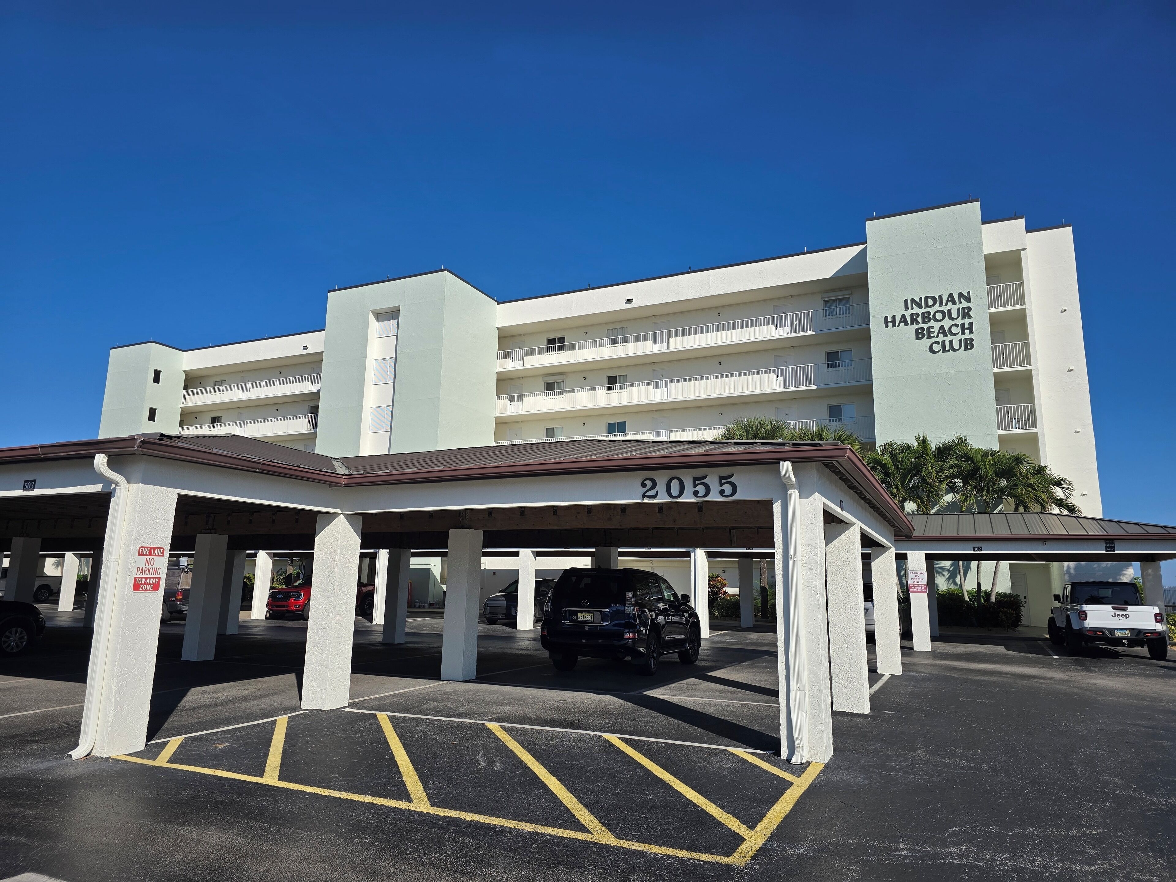 Un espace de stationnement avec, en arrière-plan, un bâtiment portant l’inscription « Indian Harbour Beach Club ».
