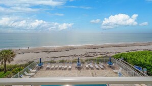 Blick auf den Strand vom Balkon mit Liegestühlen und einem Pool.