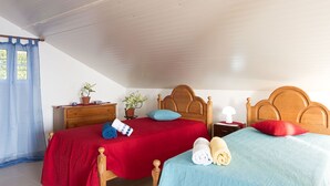 Un dormitorio con dos camas, cabeceros de madera, una mesita de noche, un aparador y dos plantas en macetas.