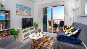 A modern living room with a flat-screen TV, a bookshelf, a coffee table, and a sofa with patterned cushions. - CH Grazalema La Marquesa Golf (Ciudad Quesada) (Ciudad Quesada)