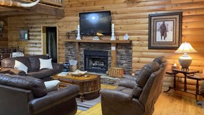A cozy log cabin interior with a fireplace, leather furniture, and a television mounted above it. - Cozy Trenton Cabin w/ Spa ~ 15 Mi to Lookout Mtn! (Trenton)