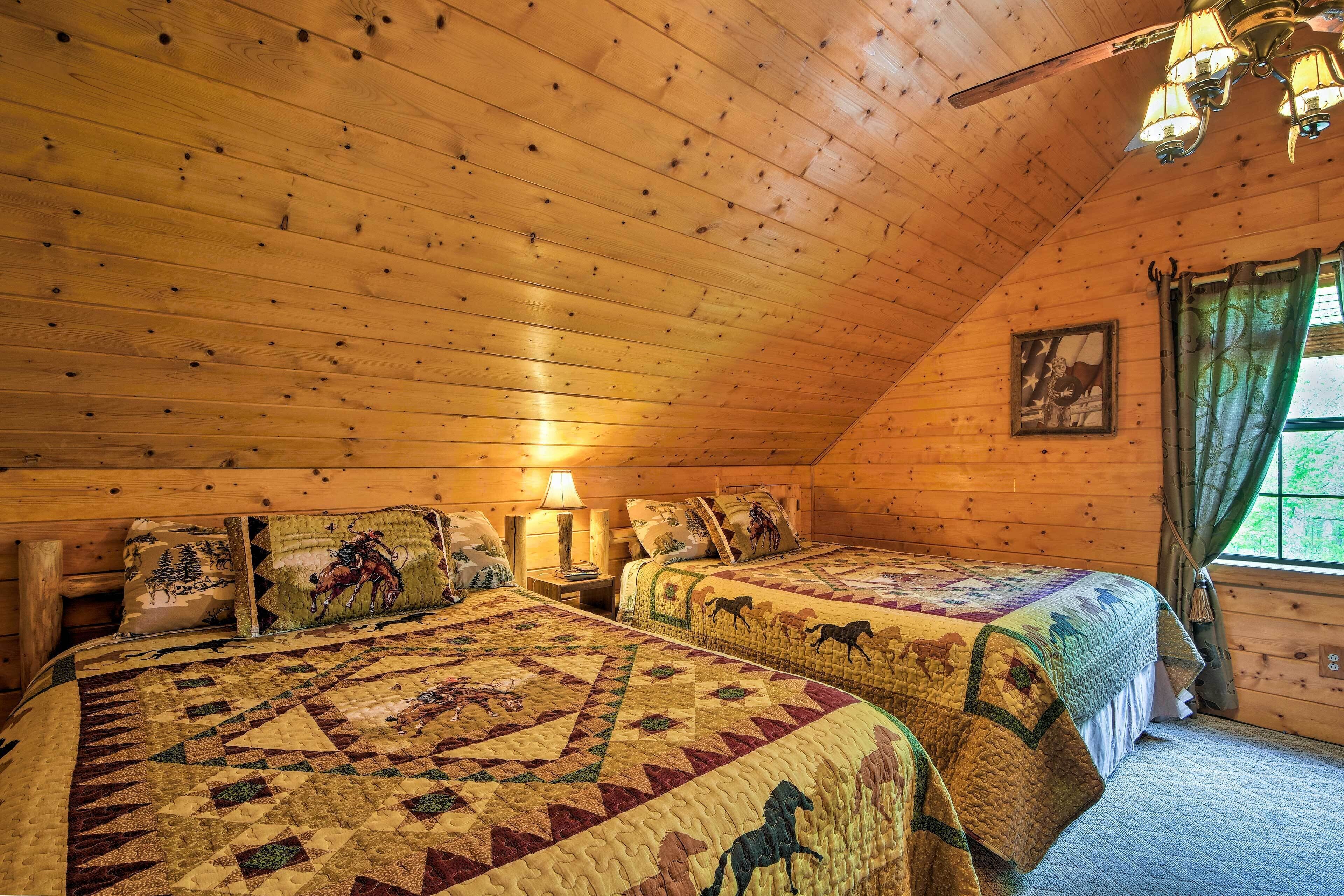 A cozy cabin room with two beds, wooden walls, a ceiling fan, and a window with curtains.